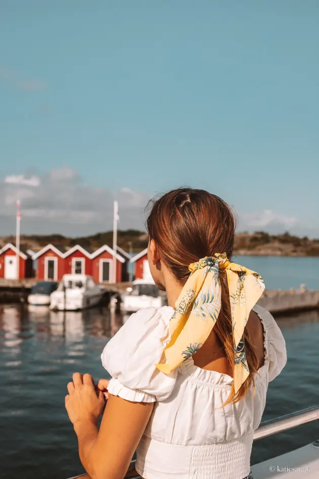 girl with a white shirt and yellow hair tie looking out over a row of red boat houses in the gothenburg archipelago